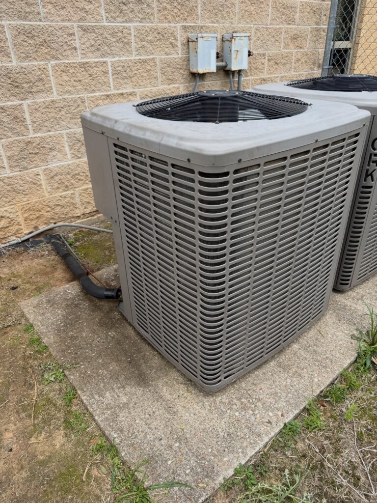 Two outdoor HVAC air conditioning condenser units mounted on concrete pads against a brick building exterior